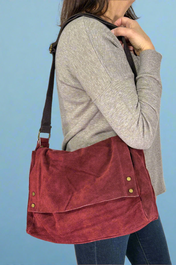 Model is wearing an Italian suede shoulder bag in a deep Bordeaux color. 