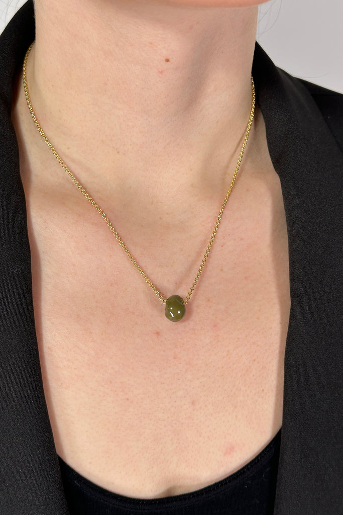 Model is wearing a gold chain collar length necklace with a small green hand rolled bead.