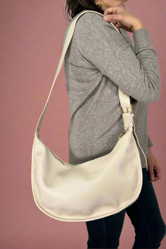 Model is holding a white hobo style crossbody bag with an adjustable strap.