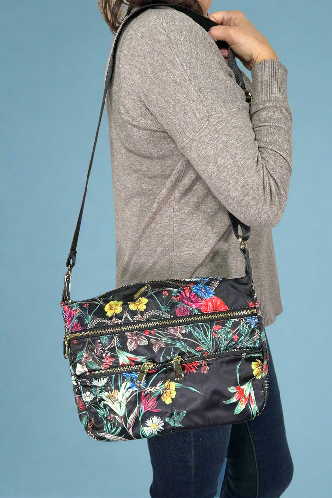 Model is holding a floral printed nylon crossbody bag with external pockets. 