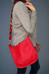 Model is wearing a bright red crossbody bag that features a metallic guitar style strap. 