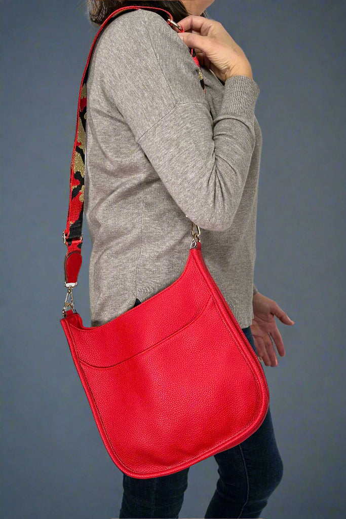 Model is wearing a bright red crossbody bag that features a metallic guitar style strap. 