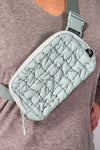 Model is wearing a sage colored quilted nylon puffer bag. 