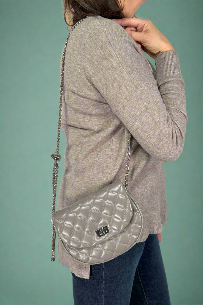 Model is wearing a grey quilted leather purse with a chainlink strap that is adjustable.