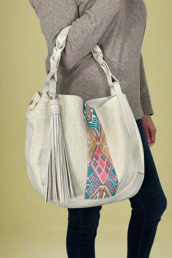 Model is holding a tribal printed saddle bag with a large tassel.