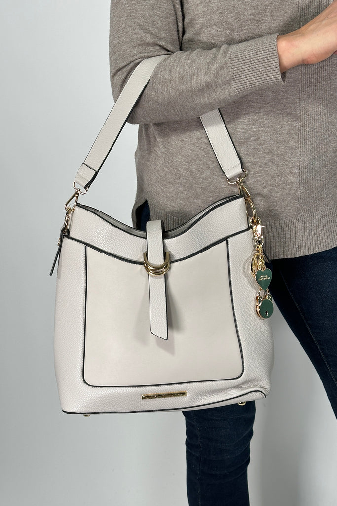 Model is holding a shoulder bag that can be converted to a crossbody. Features detachable metal charm detail.