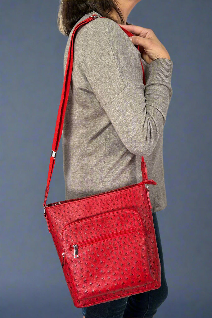 Model is holding a red faux ostrich crossbody bag with two external pockets. 