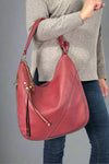 Model is holding a burgundy colored hobo bag with tassel details. 