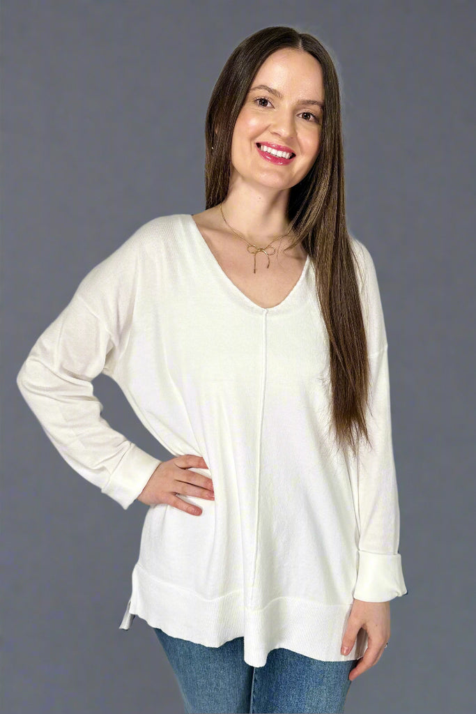 This stretchy, v-neck top is a snow white color. It has a soft texture, long sleeves, and long length.