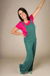 Model is wearing a hunter green jumpsuit made from ribbed fabric. It  features front pockets and button details. 