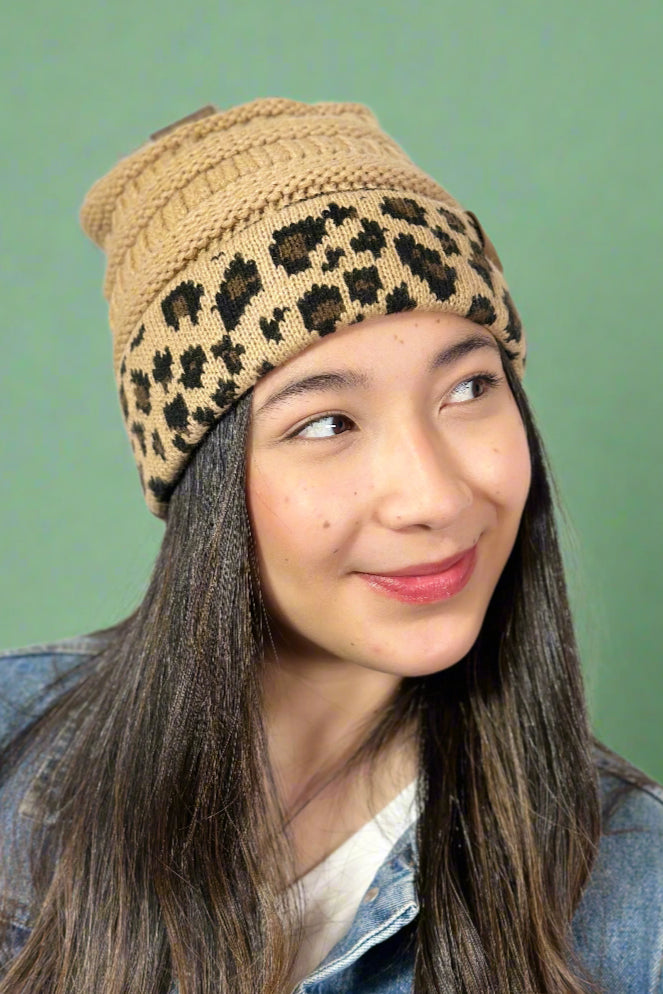 Model is wearing a tan colored cable knit beanie with a leopard printed cuff. 