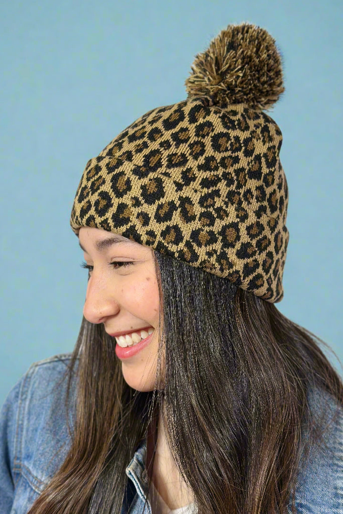 Model is wearing a leopard printed knit beanie with a pom pom on top. 