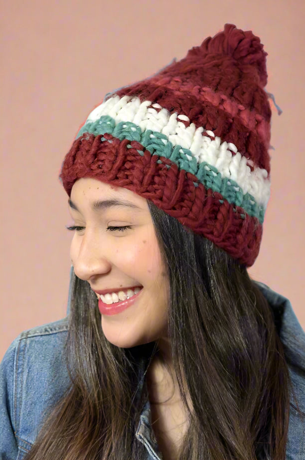 Model is wearing a striped chunky knit beanie with a large pom pom on top.