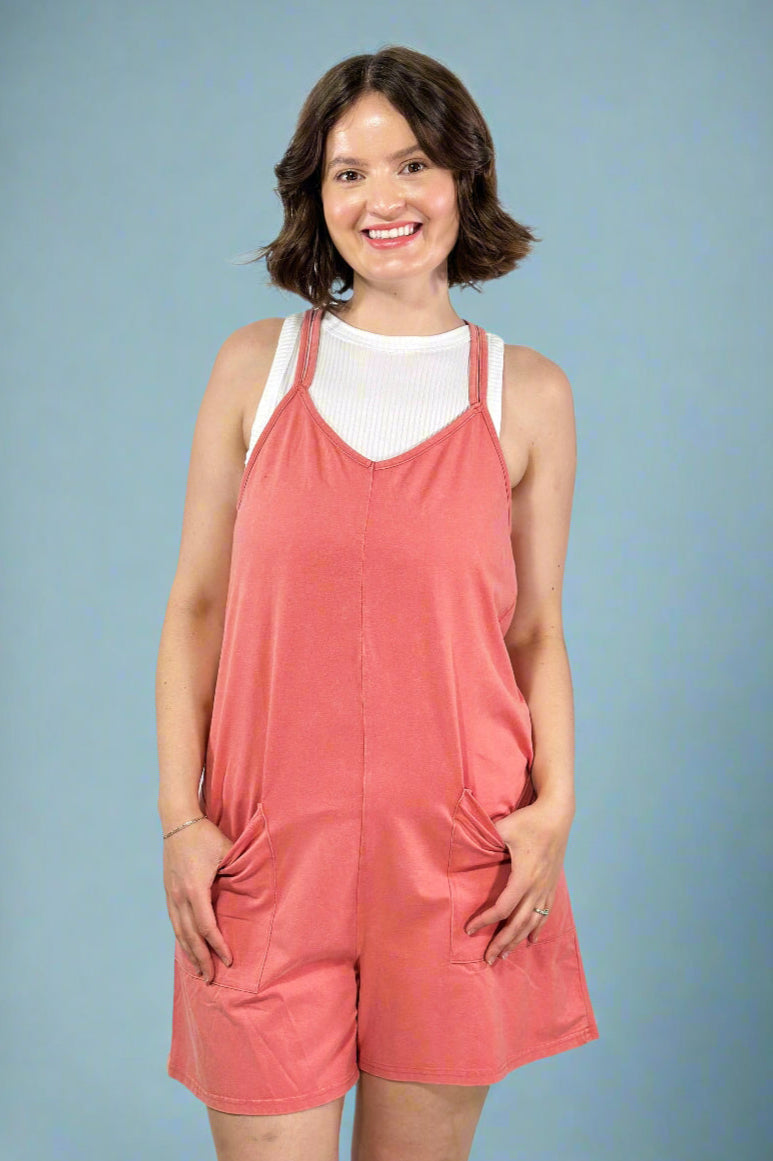 Model is wearing an orange coral colored sleeveless romper with pockets.