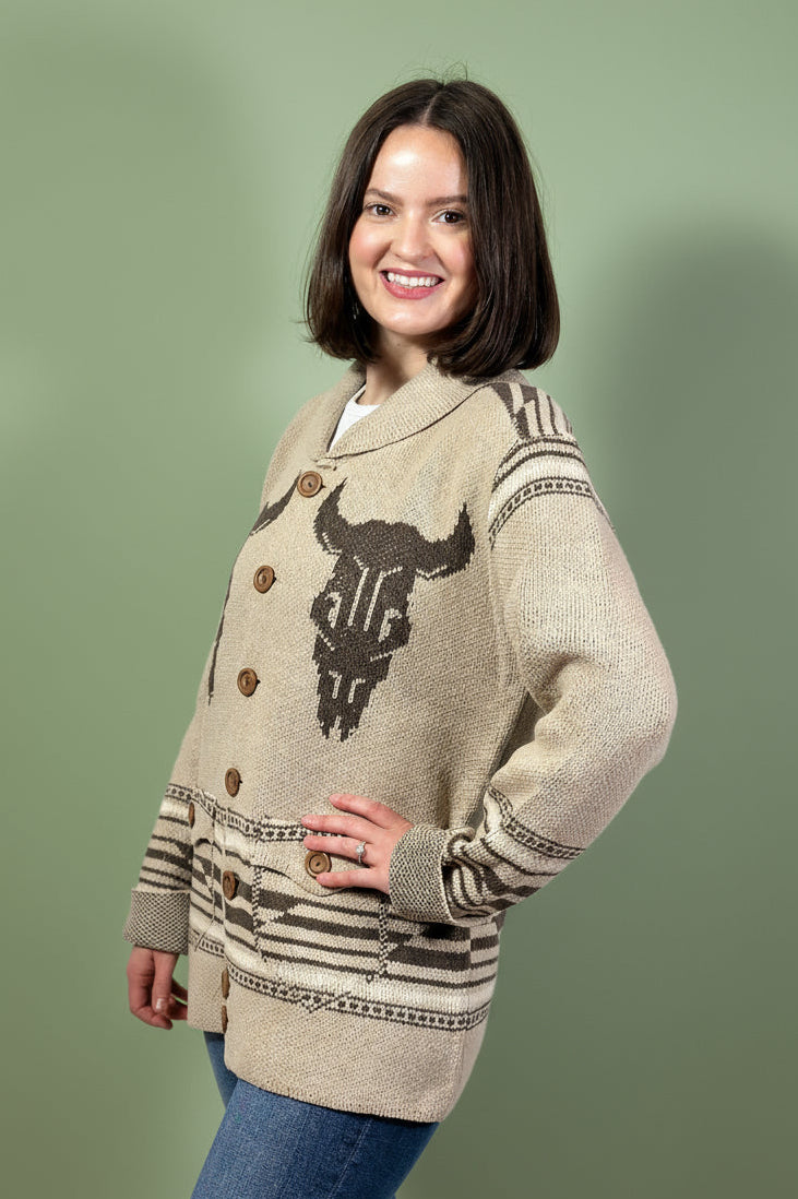 Woman wearing a patterned beige sweater with button details on a gray background