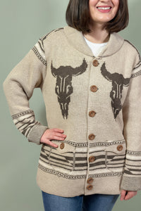 Person wearing a beige cardigan with bull skull designs on a plain background