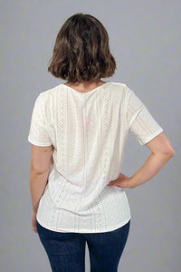 Person wearing a white blouse with short sleeves and blue jeans on a plain background