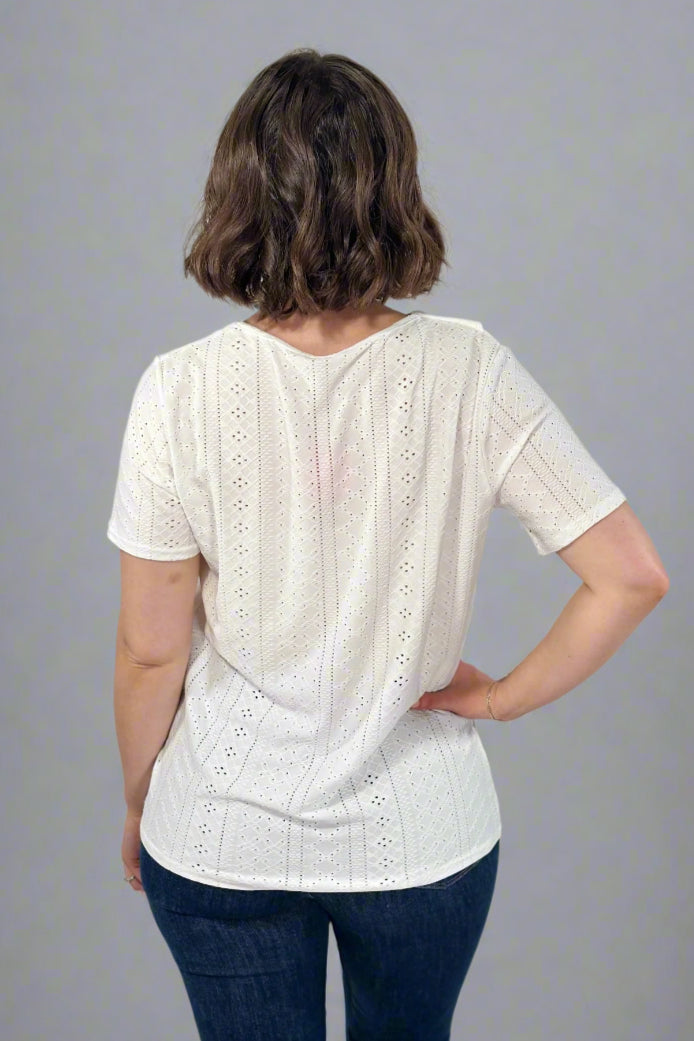 Person wearing a white blouse with short sleeves and blue jeans on a plain background