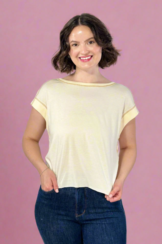 Woman wearing a beige t-shirt and blue jeans against a plain background