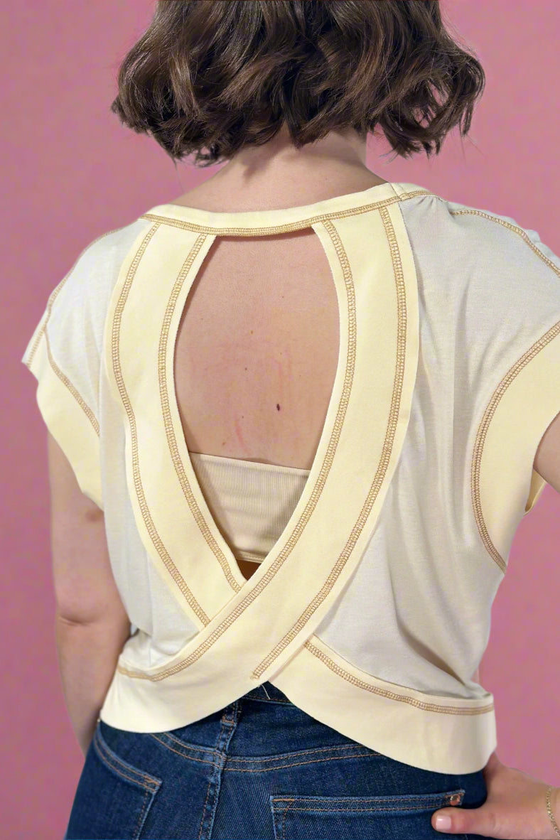 Person wearing a beige open-back top with blue jeans on a plain background