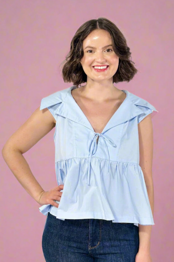 Woman wearing a light blue sleeveless top with a hood against a plain background