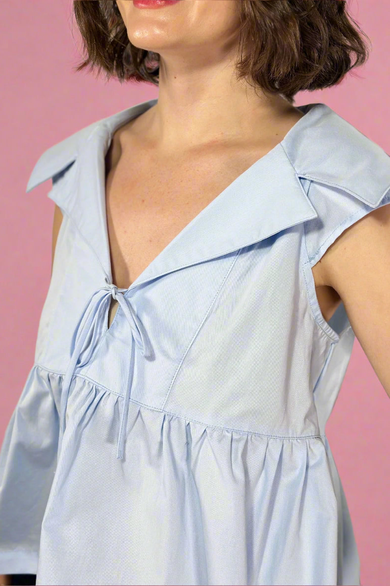 Light blue sleeveless top with ruffled collar on a neutral background