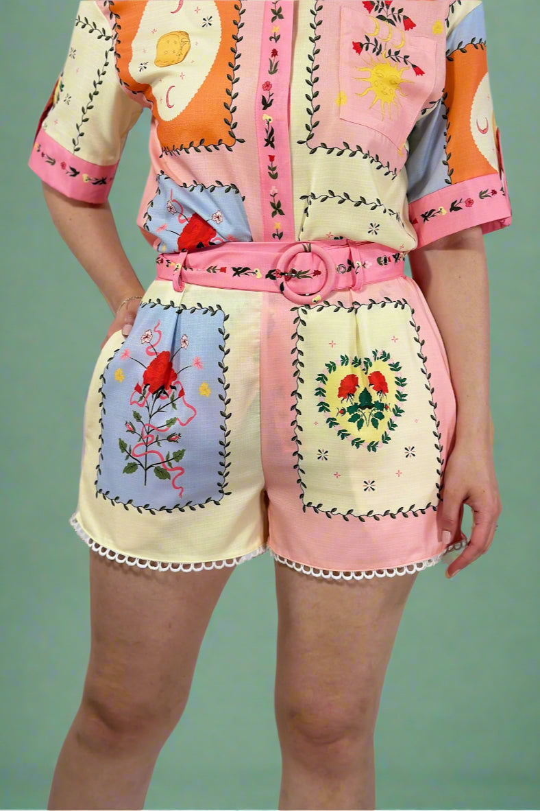 Colorful embroidered outfit with a pink belt on a plain background