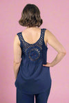 Woman wearing a navy blue sleeveless top with intricate lace detailing on the back against a plain background