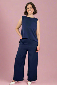 Woman wearing a navy blue sleeveless top and wide-leg pants against a white background