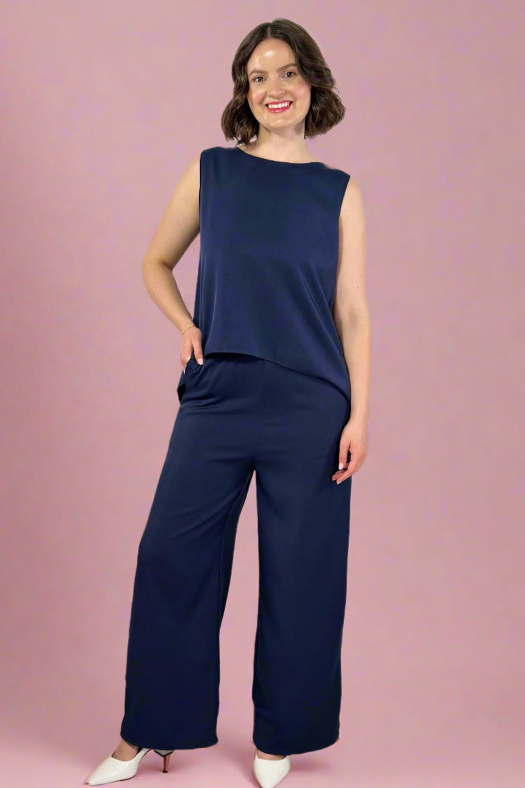 Woman wearing a navy blue sleeveless top and wide-leg pants against a white background