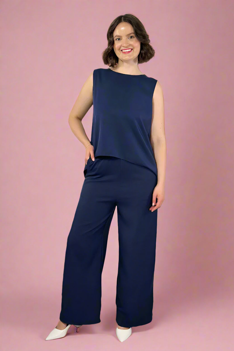Woman wearing a navy blue sleeveless top and wide-leg pants against a white background