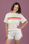 Woman wearing a white t-shirt with colorful stripes and white shorts on a gray background