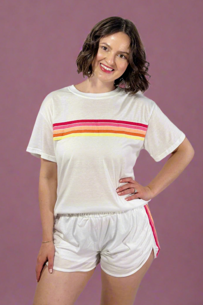 Woman wearing a white t-shirt with colorful stripes and white shorts on a gray background