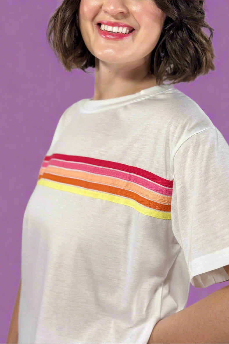 Person wearing a white t-shirt with colorful horizontal stripes on a plain background