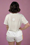 Person wearing a white t-shirt and shorts with a logo on the back, standing against a plain background.