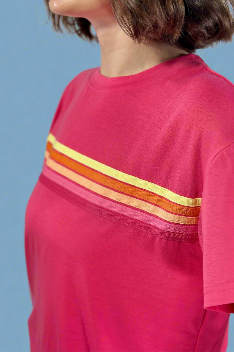 Close-up of a person wearing a pink t-shirt with orange and yellow stripes on a plain background