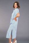 Woman wearing an oversized striped cream and light blue button down midi dress with pockets. Cuffed short sleeves.