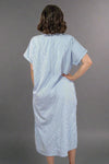 Woman wearing an oversized striped cream and light blue button down midi dress with pockets. Cuffed short sleeves.