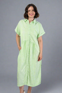 Woman wearing an oversized striped cream and light green button down midi dress with pockets. Cuffed short sleeves.
