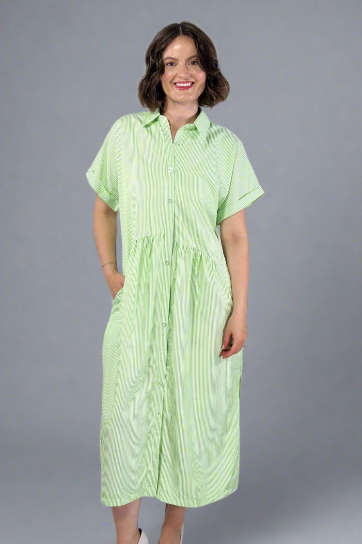 Woman wearing an oversized striped cream and light green button down midi dress with pockets. Cuffed short sleeves.