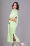 Woman wearing an oversized striped cream and light green button down midi dress with pockets. Cuffed short sleeves.