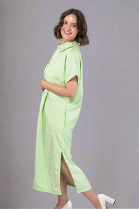 Woman wearing an oversized striped cream and light green button down midi dress with pockets. Cuffed short sleeves.