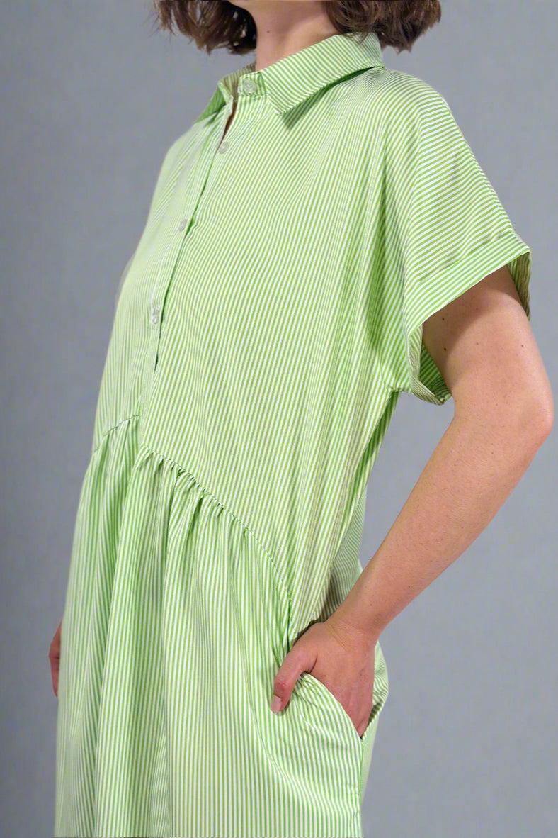 Woman wearing an oversized striped cream and light green button down midi dress with pockets. Cuffed short sleeves.