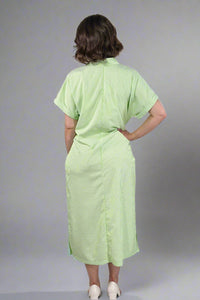 Woman wearing an oversized striped cream and light green button down midi dress with pockets. Cuffed short sleeves.