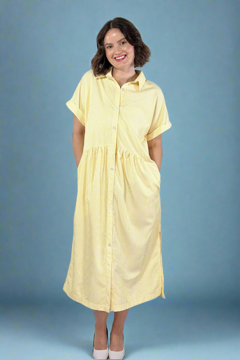 Woman wearing a oversized striped cream and yellow button down midi dress with pockets.