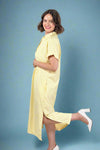 Woman wearing an oversized striped cream and yellow button down midi dress with pockets. Cuffed short sleeves.