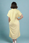 Woman wearing an oversized striped cream and yellow button down midi dress with pockets. Cuffed short sleeves.