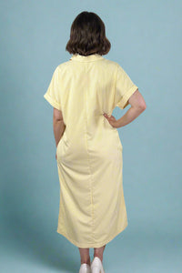 Woman wearing an oversized striped cream and yellow button down midi dress with pockets. Cuffed short sleeves.