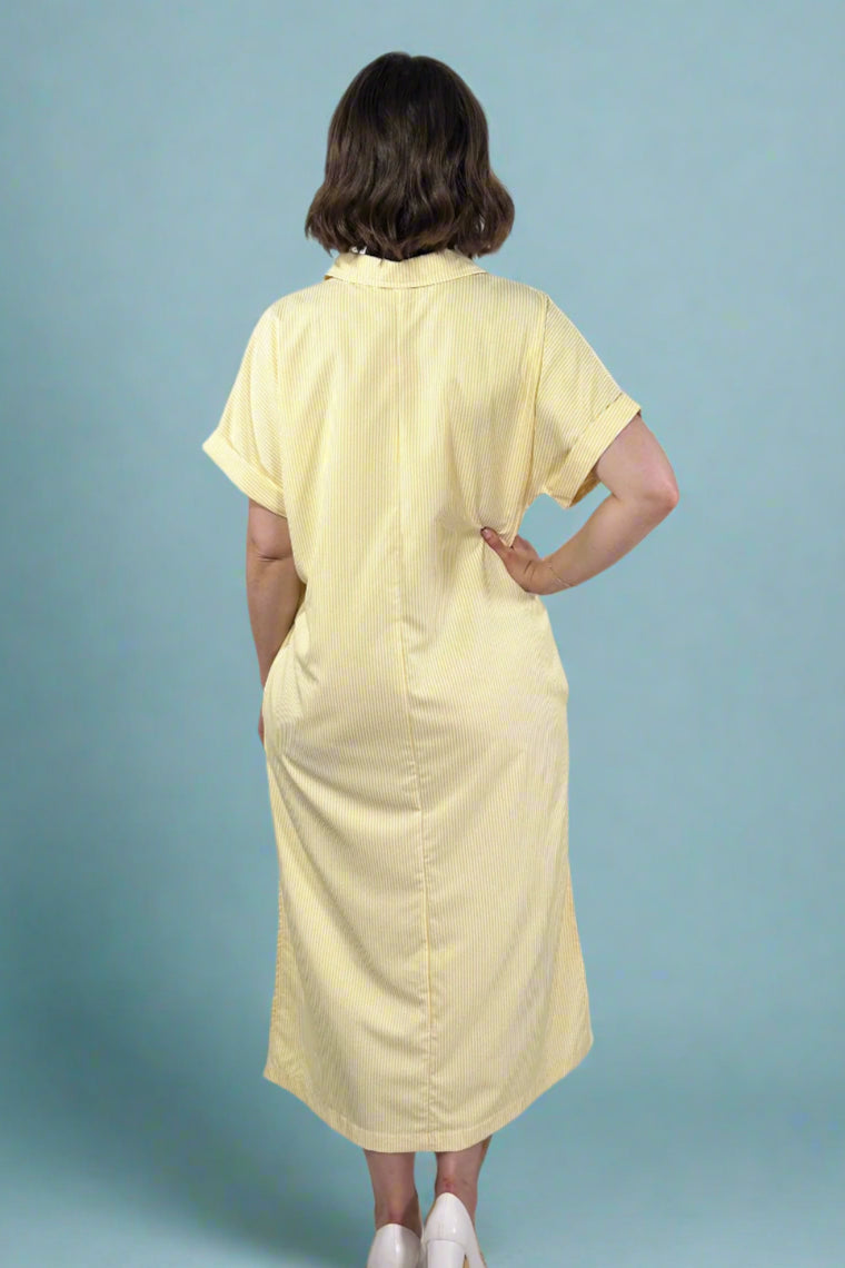 Woman wearing an oversized striped cream and yellow button down midi dress with pockets. Cuffed short sleeves.