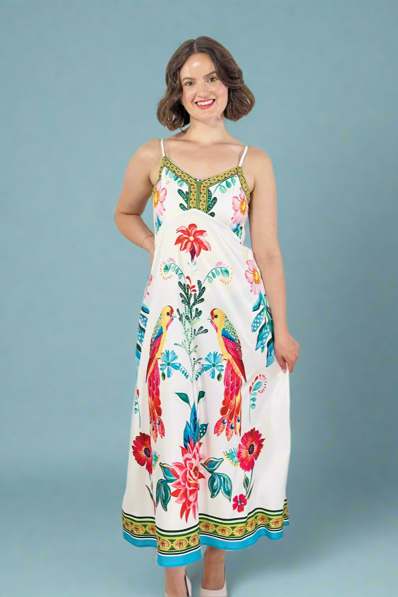 Woman wearing a colorful dress with parrot and floral patterns on a plain background